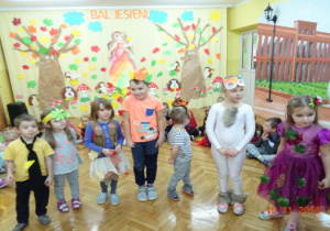 Dzieci stoją w rzędzie w jesiennych przebraniach.